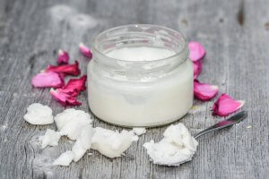 coconut oil in spoon with open coconut oil jar and petals around it