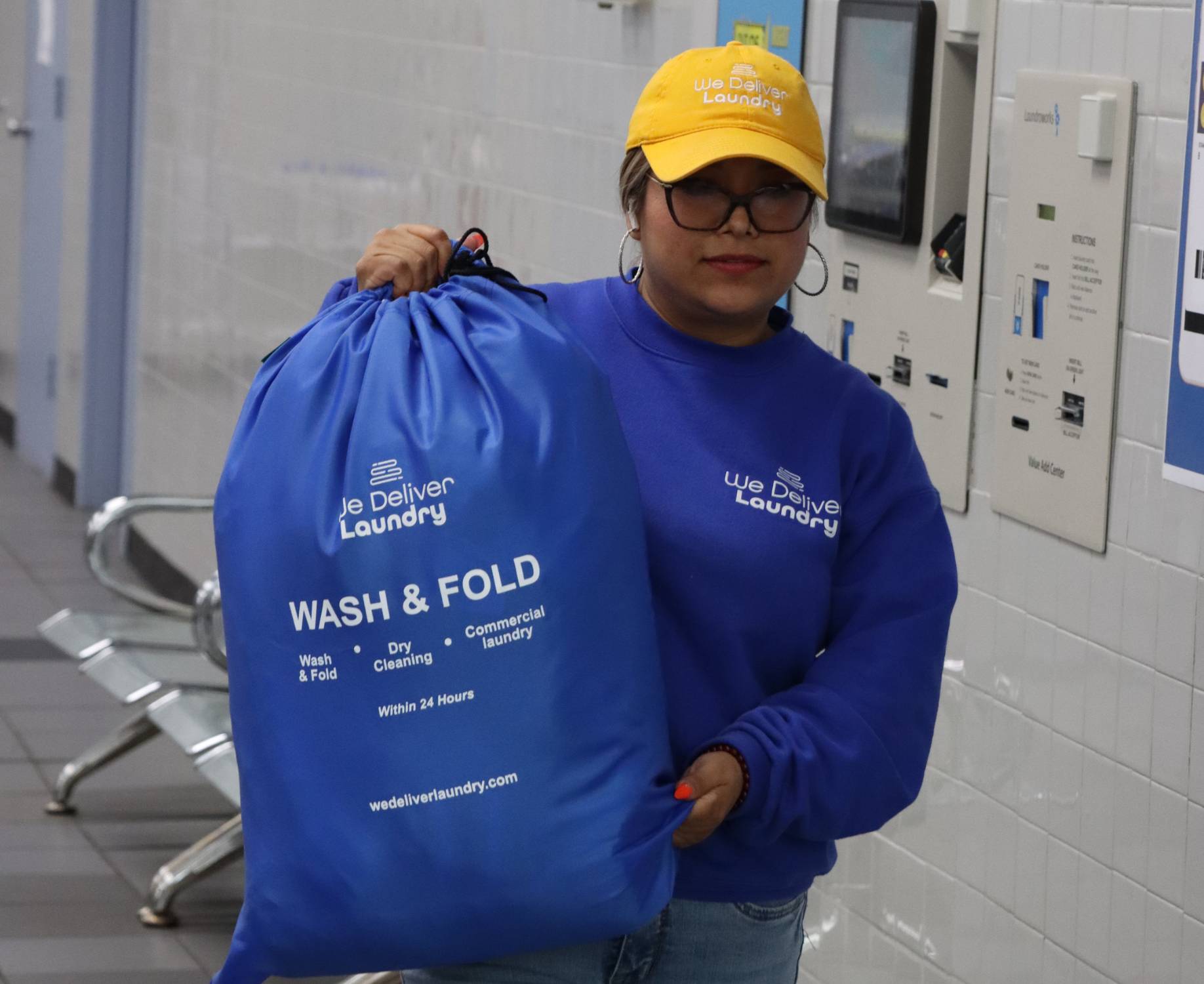 We Deliver Laundry team member carrying a blue Wash & Fold laundry bag inside a professional laundry facility.